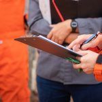 professional safety consultant talking to a group of working with a clipboard in hand